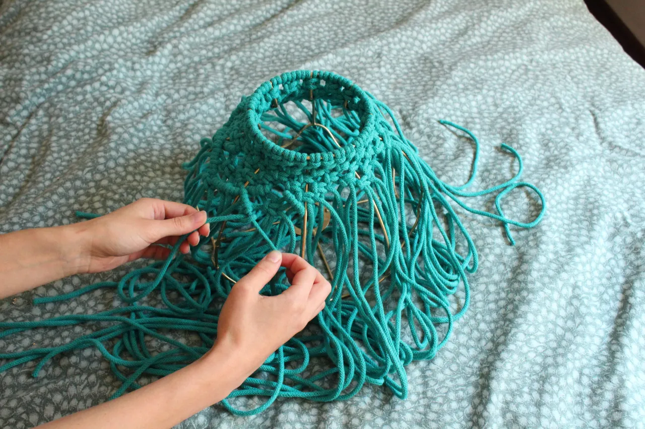 Ręce tworzą turkusowy abażur techniką makramy. Dowiedz się, jak zrobić stylowy abażur krok po kroku.
