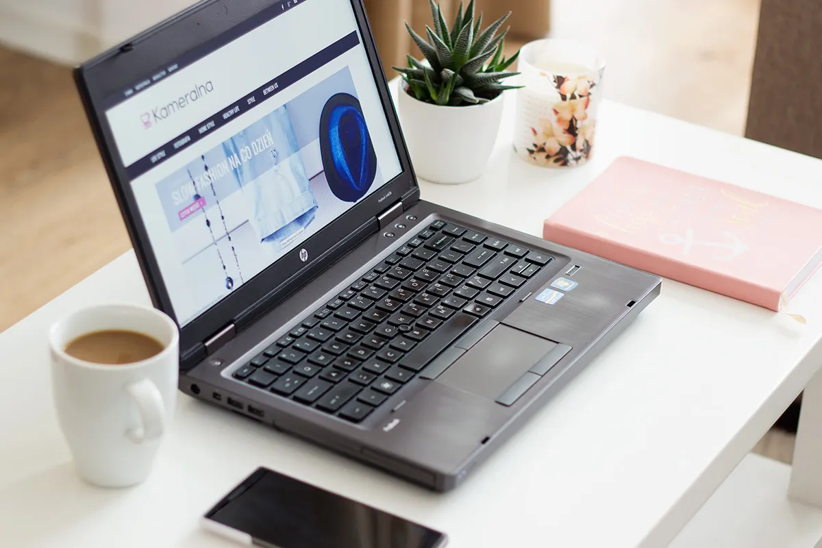 Laptop z otwartą stroną bloga, filiżanka kawy i notatnik. Inspiracja, jak pisać bloga przykłady.