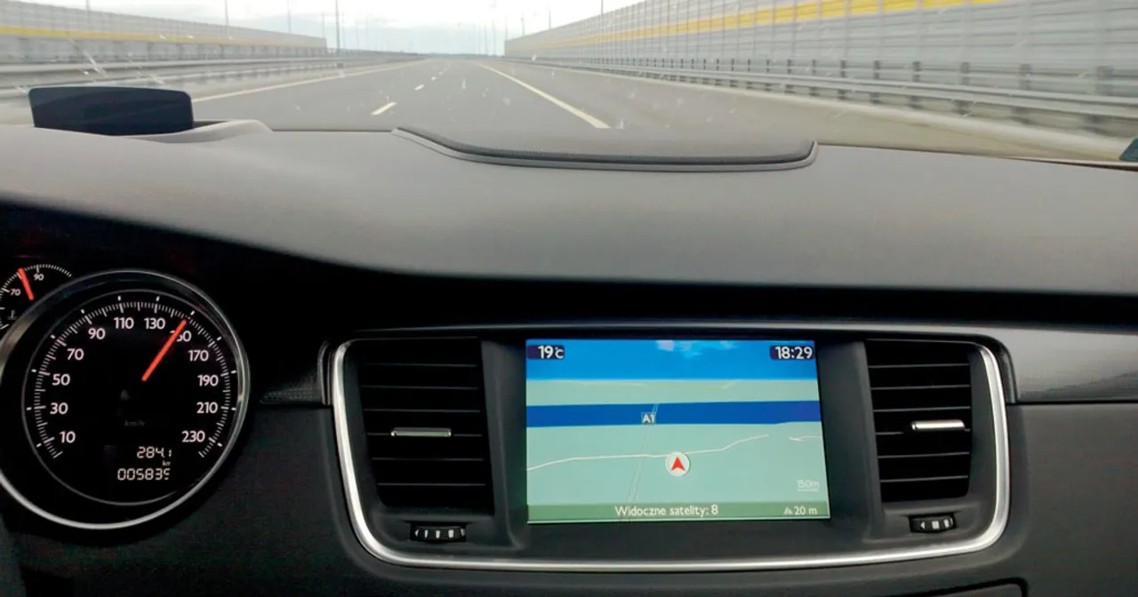 Widok z kabiny samochodu na autostradę. Na desce rozdzielczej nawigacja pokazuje trasę, a obok prędkościomierz. Jak zaktualizować mapę w nawigacji?