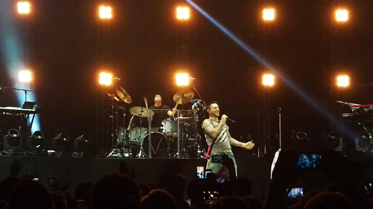 Adam Levine śpiewa na koncercie Maroon 5. Widownia nagrywa występ, zastanawiając się, ile trwa koncert Maroon 5.