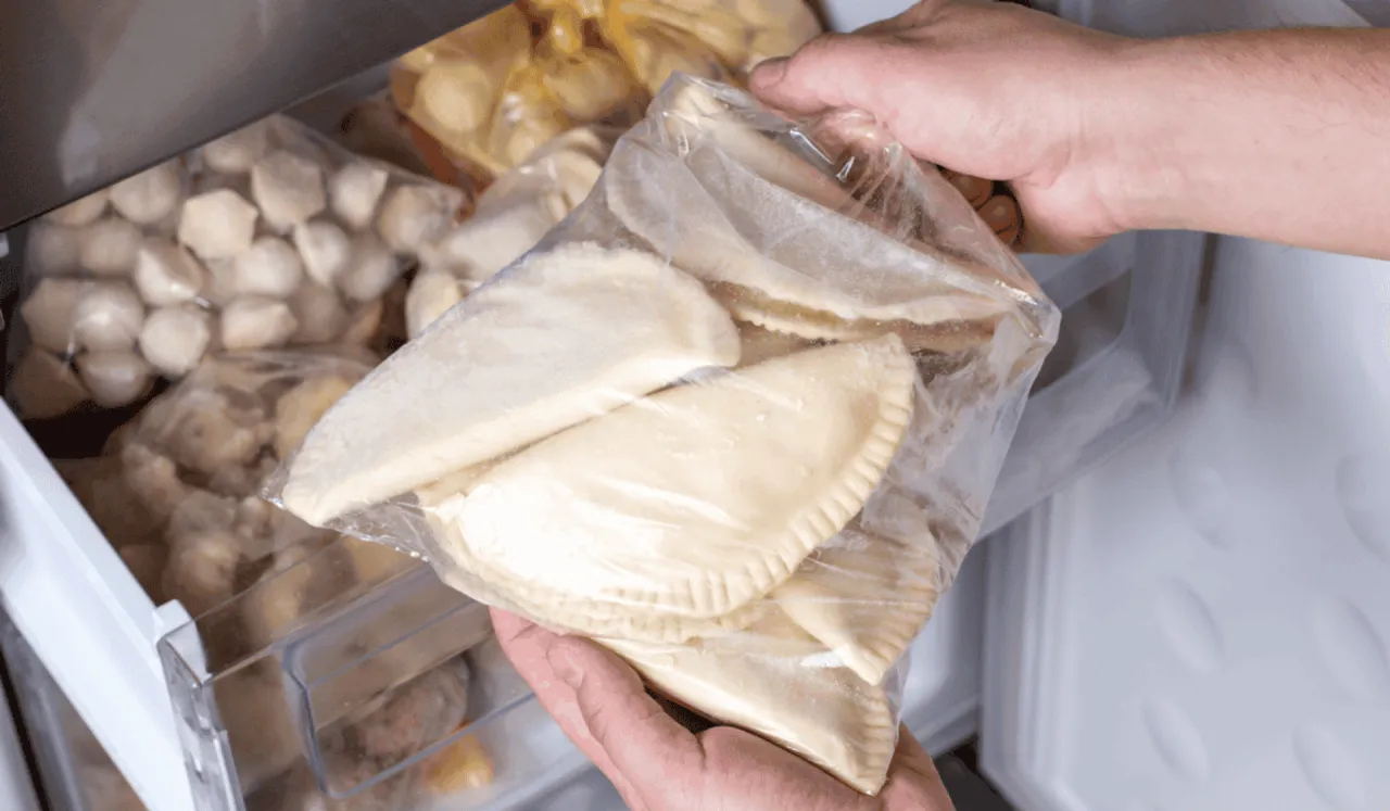 Ręce wkładają do zamrażarki worek z surowymi pierogami. To prosty sposób, jak mrozić pierogi, by cieszyć się nimi później.