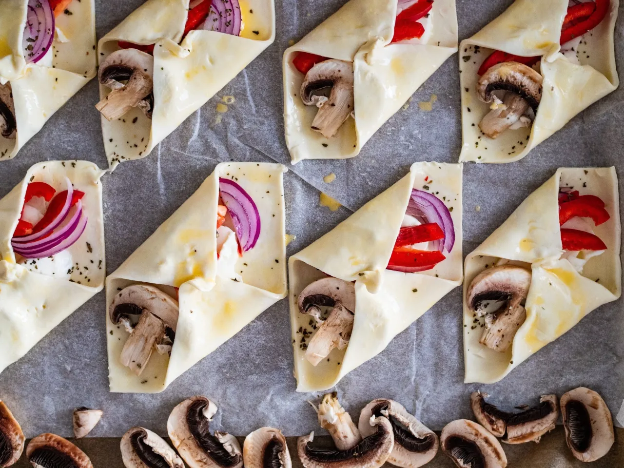 Oto jak zawijać ciasto francuskie: przygotowane kawałki ciasta z pieczarkami, papryką i cebulą czekają na pieczenie.