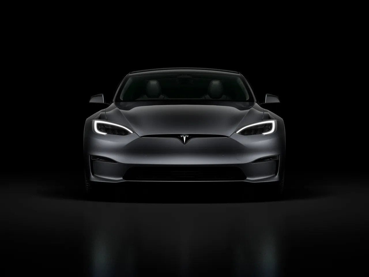 Szary Tesla Model S z włączonymi światłami, prezentujący nowoczesny design. Tesla co to? To przyszłość motoryzacji.