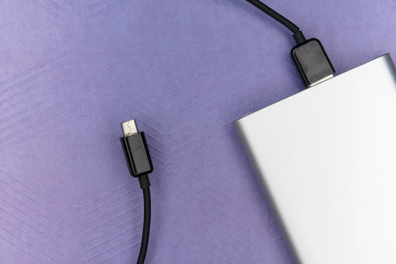 Srebrny powerbank i kabel USB na fioletowym tle. Zastanawiasz się, czy powerbanki o dużej pojemności można przewozić w samolocie?
