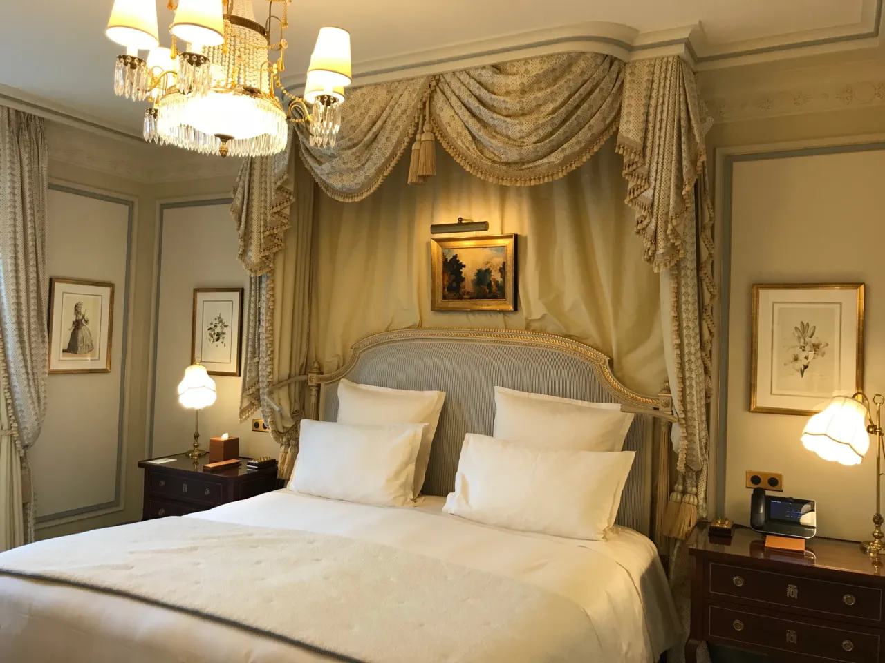 Elegancka sypialnia w hotelu Ritz w Paryżu. Luksusowe łóżko z baldachimem, kryształowy żyrandol i zabytkowe obrazy tworzą atmosferę królewskiego splendoru.