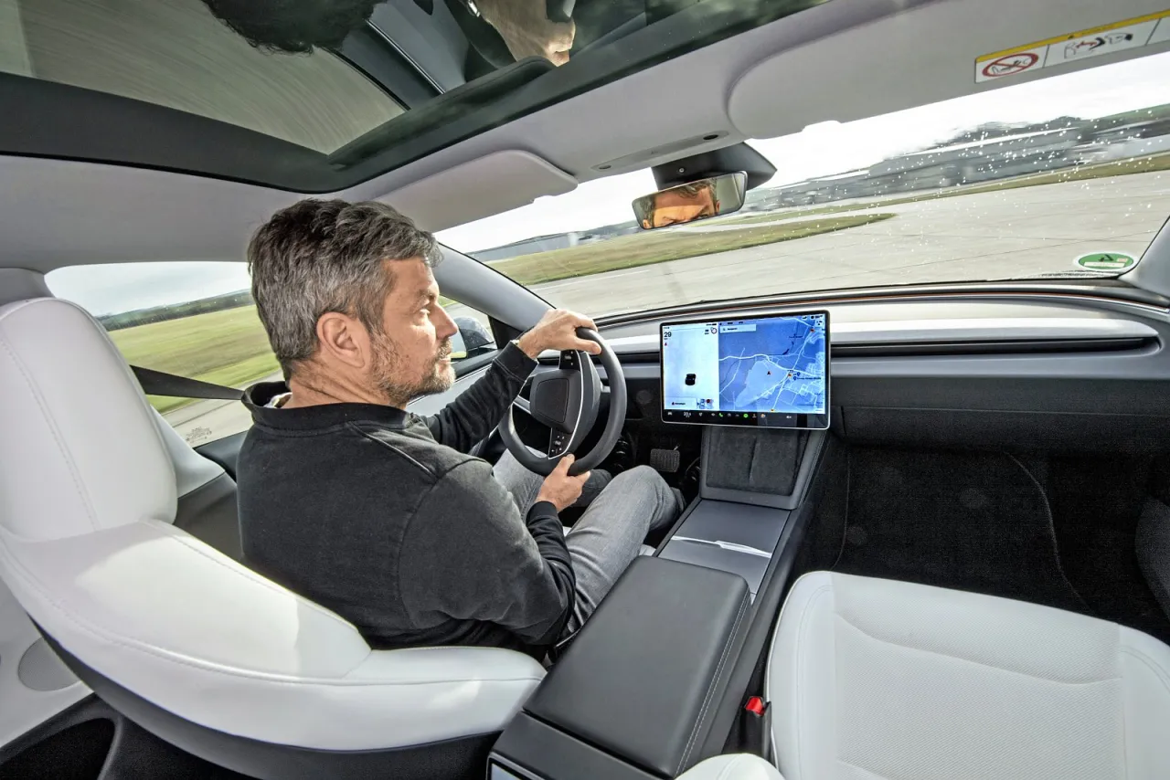 Mężczyzna za kierownicą Tesli, zastanawia się, ile kosztuje najtańsza Tesla, podczas jazdy po torze.