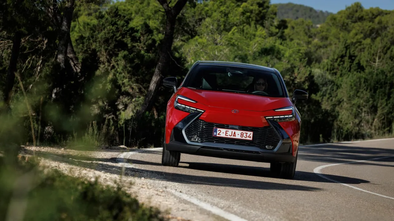 Czerwona Toyota C-HR na krętej drodze wśród zieleni. Zastanawiasz się, ile kosztuje nowa Toyota C-HR?