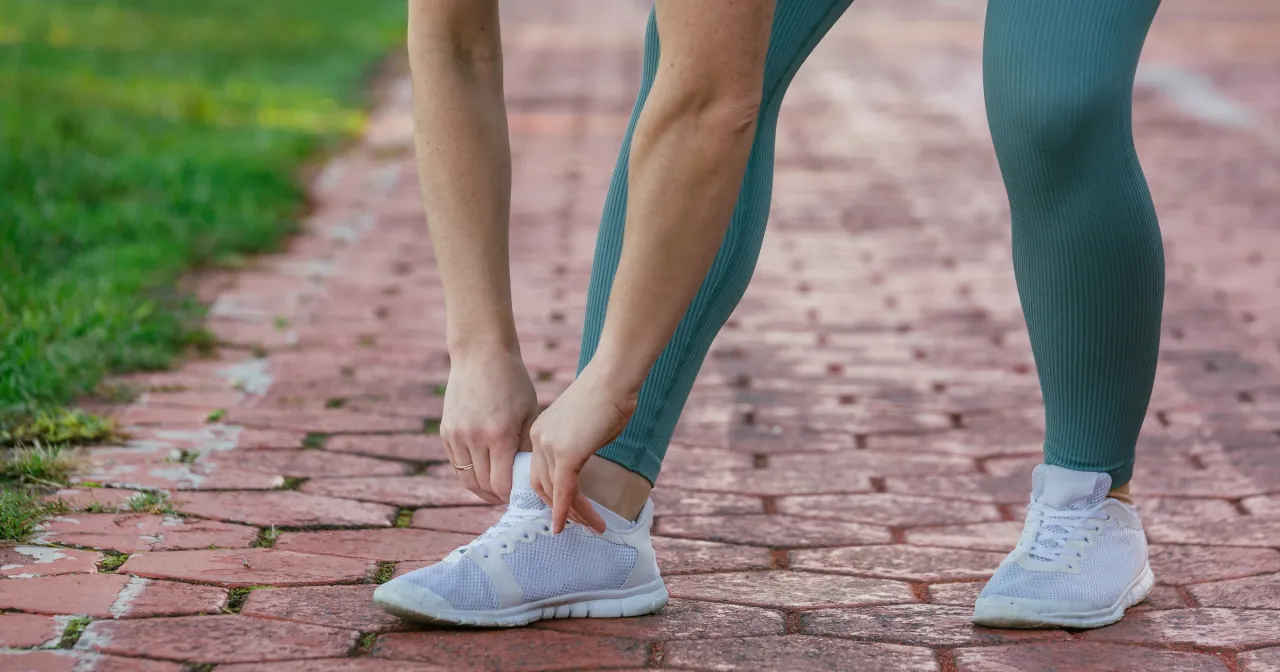 Kobieta wiąże sznur&oacute;wki białych but&oacute;w na ścieżce z czerwonej kostki brukowej. To dow&oacute;d, że czy codzienny trening ma sens.