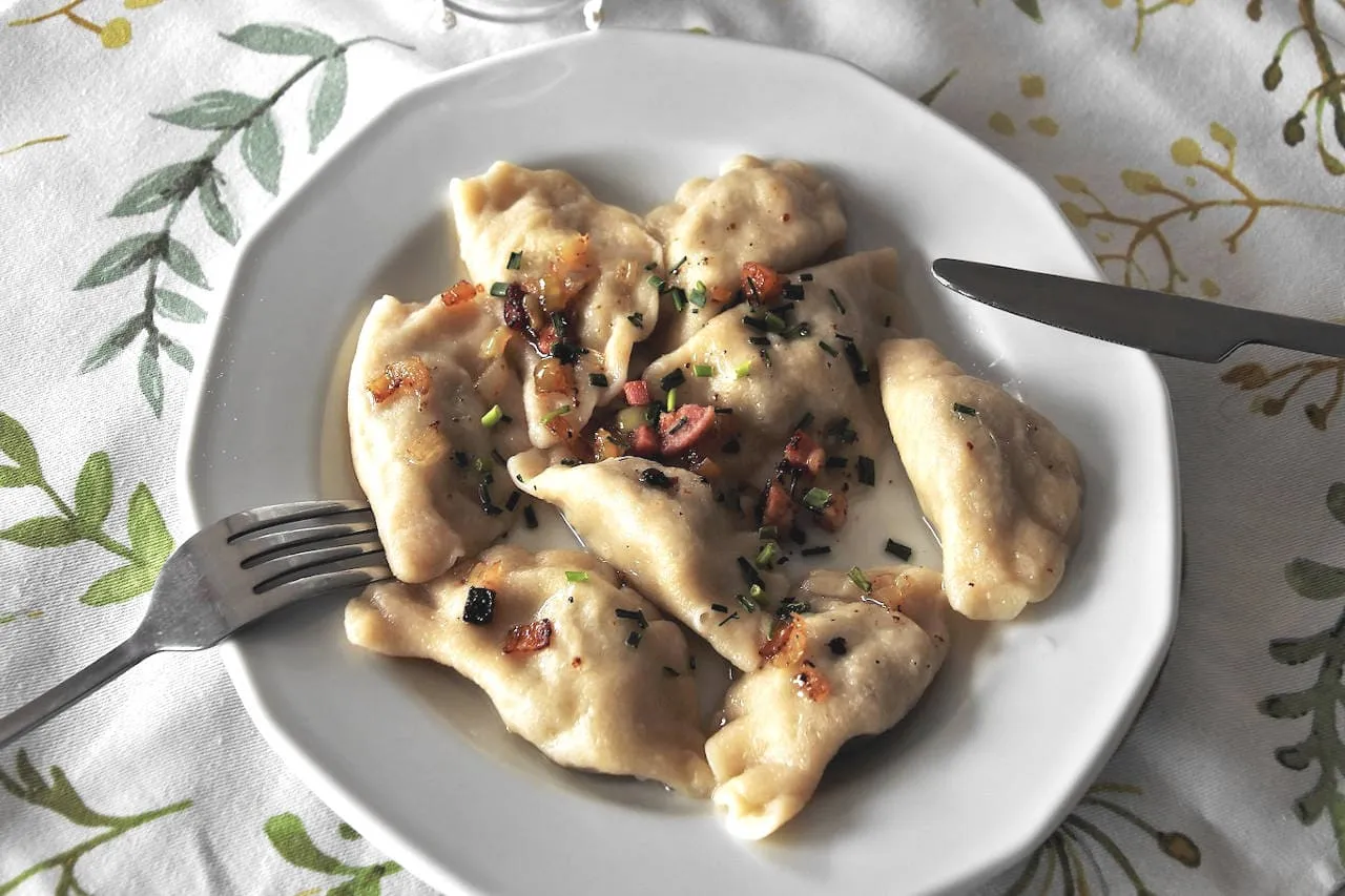 Talerz pysznych pierogów okraszonych skwarkami i szczypiorkiem. Zastanawiasz się, ile sztuk pierogów wchodzi na kilogram?