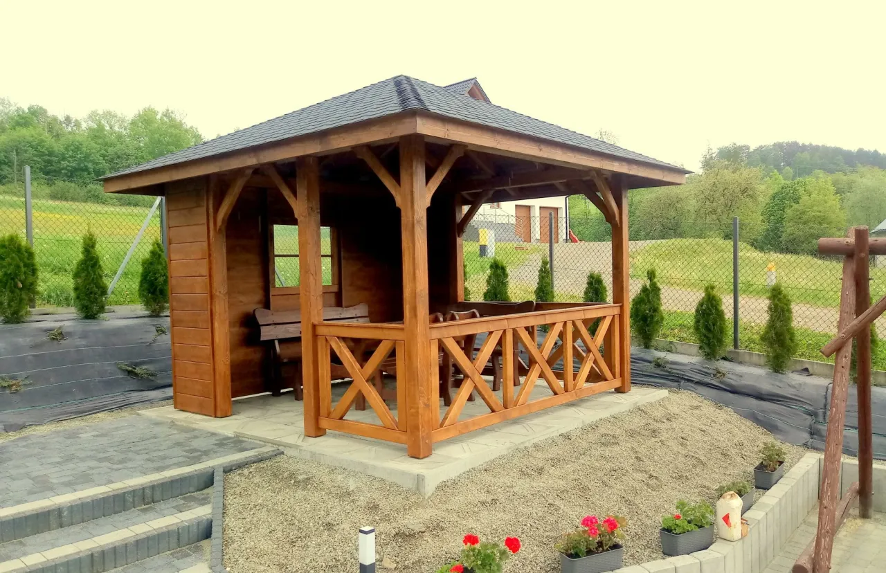 Drewniana altana 3x3 z gontem na dachu, otoczona zielenią i ogrodzeniem.