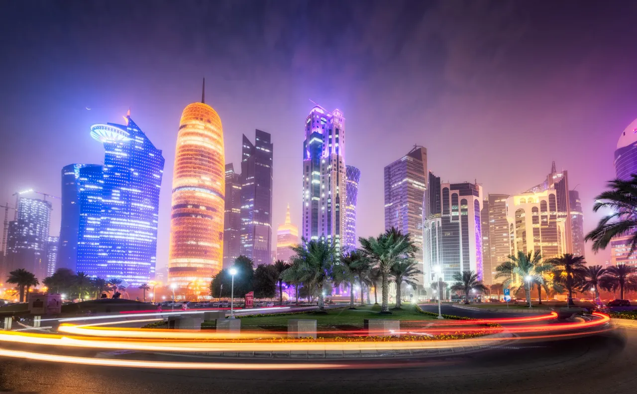 Nocny widok na drapacze chmur w Katarze, gdzie leży Doha. Rozświetlone budynki i smugi świateł samochod&oacute;w tworzą futurystyczny krajobraz.