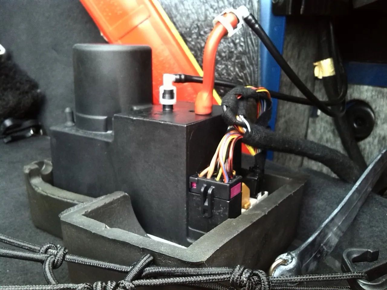 Pompka centralnego zamka Audi A4 B5, zlokalizowana w bagażniku, obok pomarańczowego trójkąta ostrzegawczego.