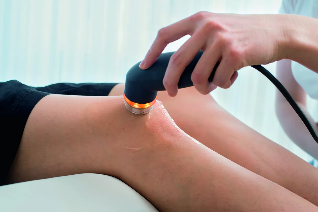 Rehabilitacja ultradźwięki na czym polega? Fizjoterapeuta wykonuje zabieg ultradźwiękami na kolanie pacjenta, co pomaga w leczeniu bólu i przyspiesza regenerację.