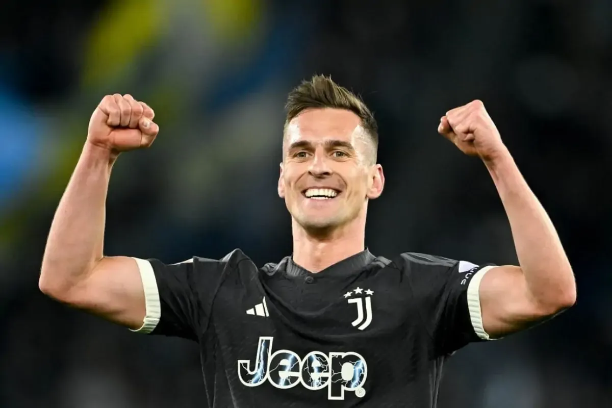Piłkarz w czarnej koszulce Juventusu z podniesionymi pięściami. Uśmiecha się radośnie. Ciekawe, ile zarabia Milik.