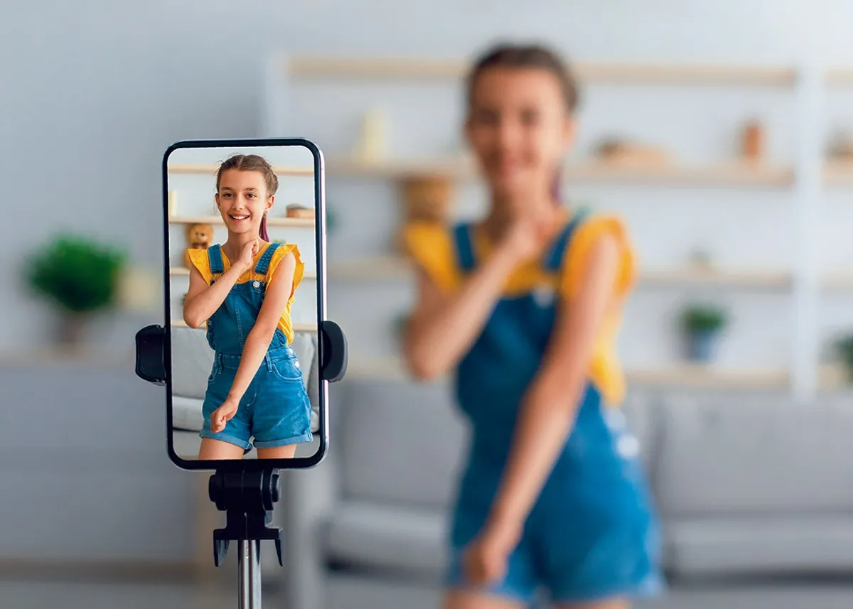 Uśmiechnięta dziewczynka w ogrodniczkach na ekranie telefonu. Zastanawiasz się, ile zarabiają dzieci influencerów za udział w kampaniach reklamowych?