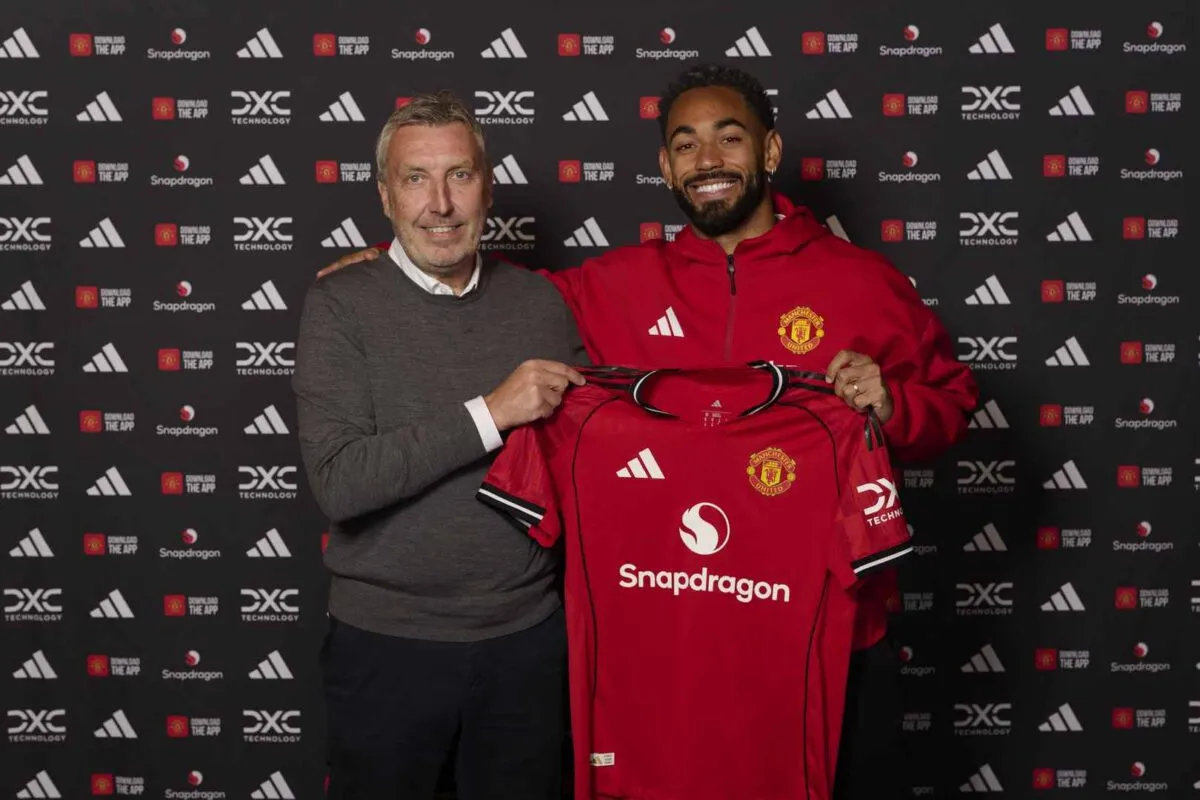 Dwóch mężczyzn prezentuje nową koszulkę Manchester United. Jeden z nich, ubrany w szary sweter, trzyma koszulkę, a drugi, w czerwonej bluzie, stoi obok. To część prezentacji nowego składu Manchester United.