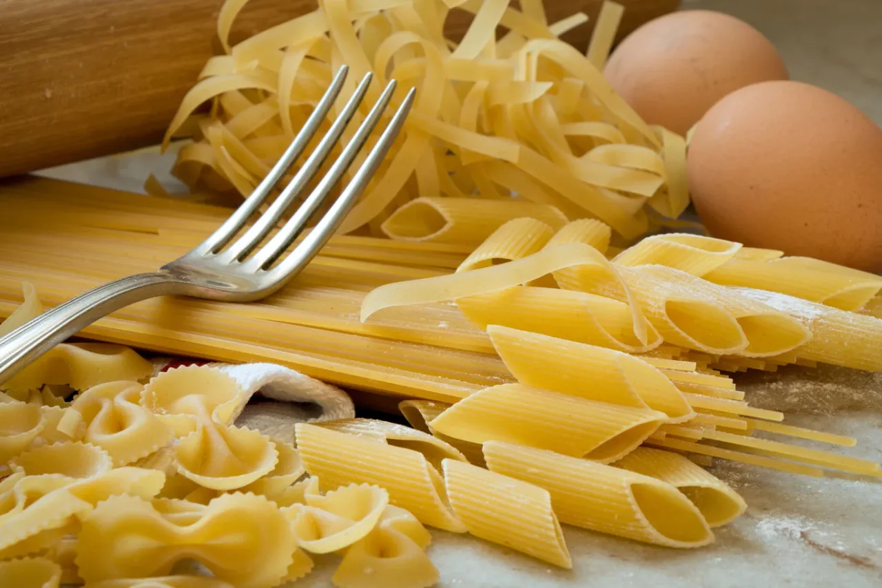 Różne rodzaje makaronu, jajka i wałek do ciasta. Idealne składniki, by dowiedzieć się, jak zamrozić ugotowany makaron.