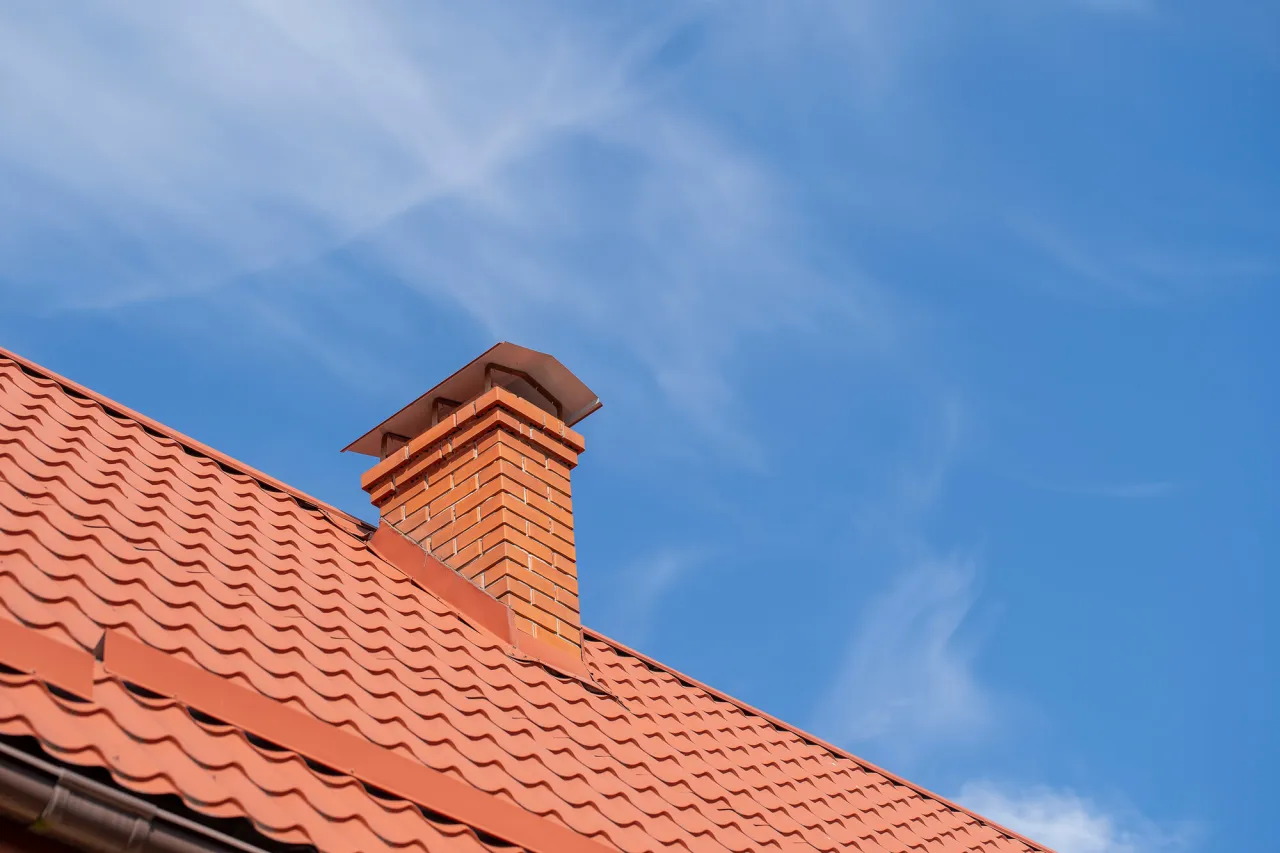 Ceglany komin na dachu z dach&oacute;wką. Pokazano, jak obrobić komin blachą, by chronić go przed deszczem.