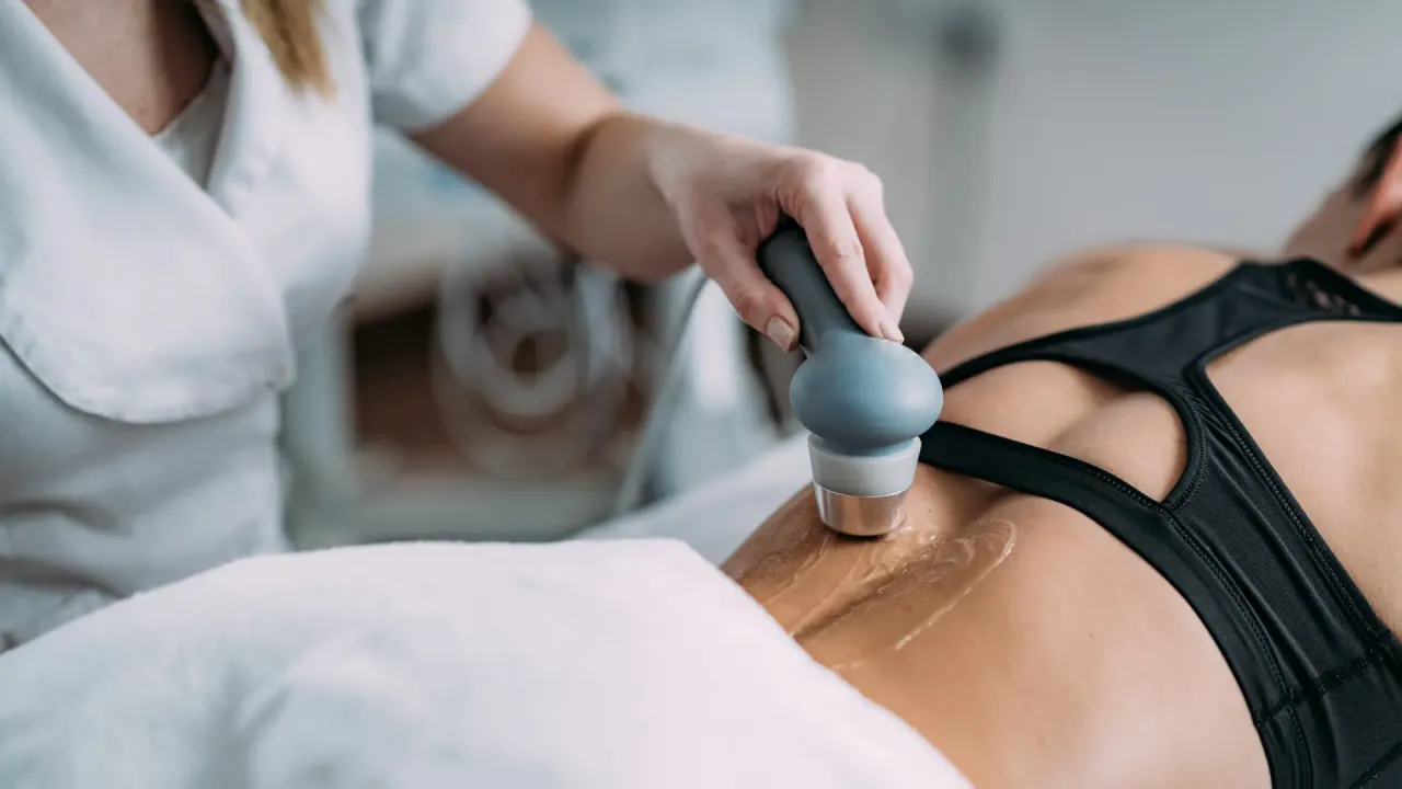 Rehabilitacja ultradźwięki na czym polega? Fizjoterapeuta wykonuje zabieg ultradźwiękami na plecach pacjentki, co pomaga w leczeniu bólu i regeneracji tkanek.