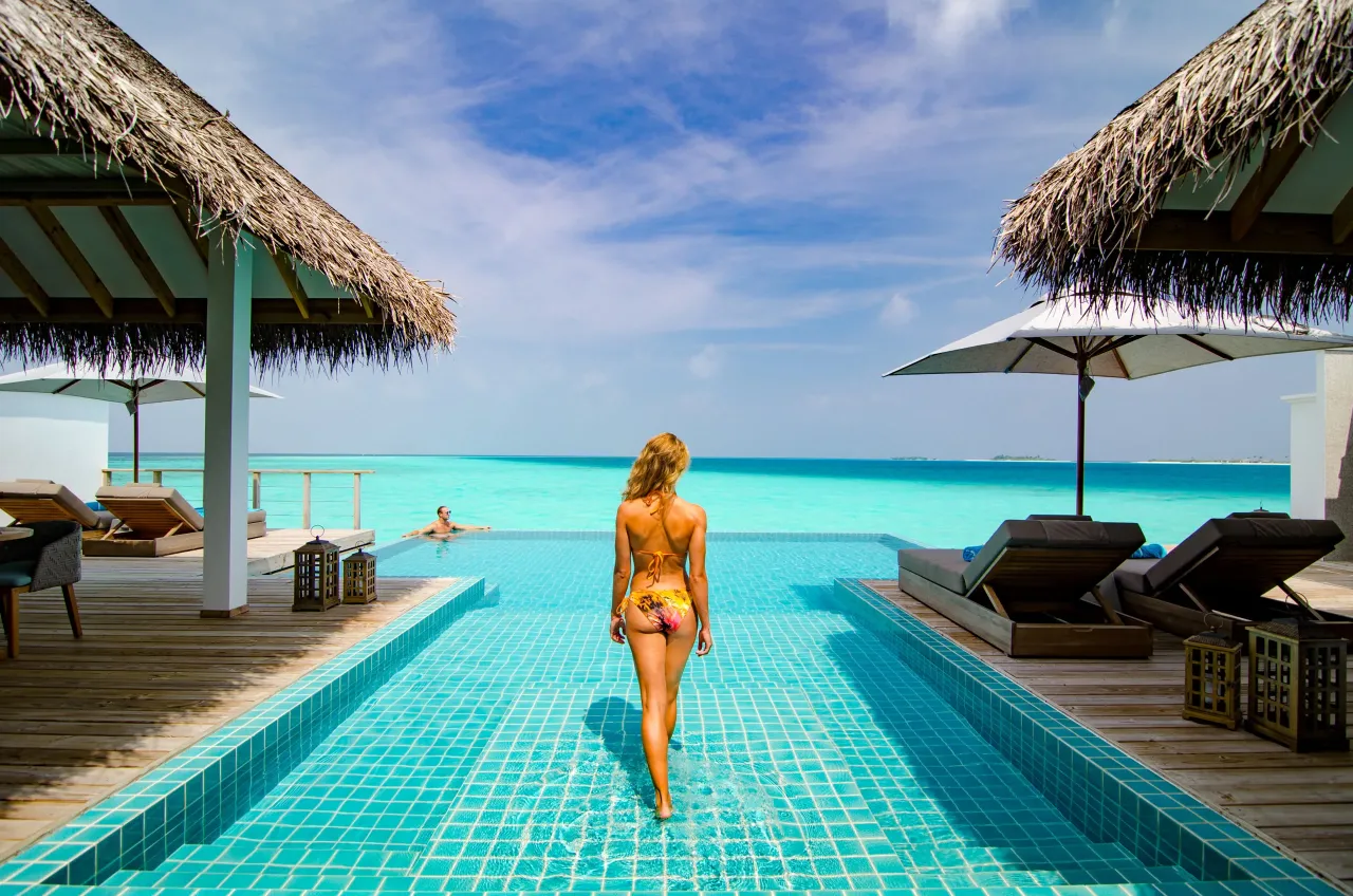 Malediwy domki na wodzie ze zjeżdżalnią, basen i turkusowe morze. Kobieta w bikini wchodzi do wody.