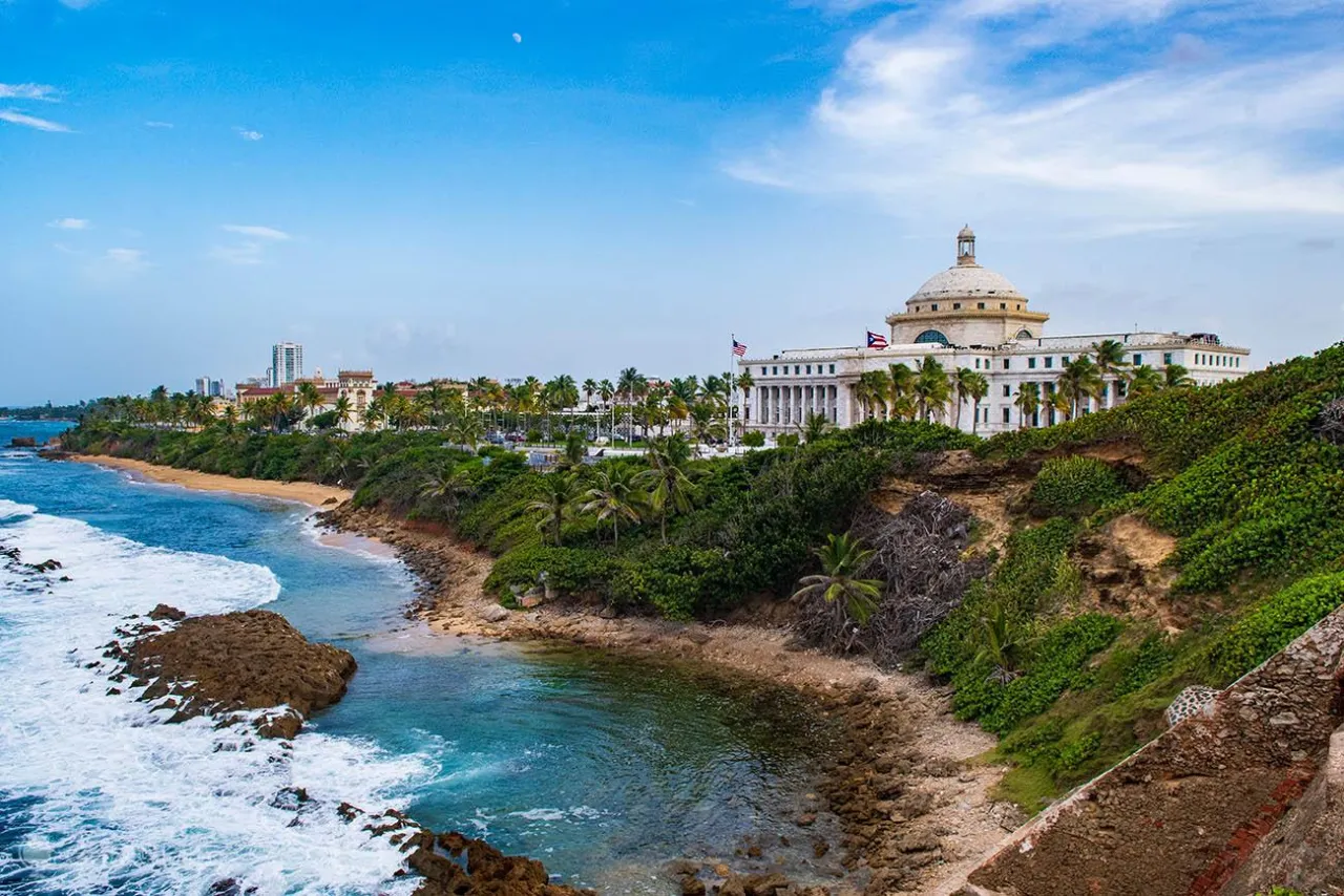 Widok na wybrzeże z budynkiem Kapitolu, gdzie leży Puerto Rico. Błękitne morze, plaża i palmy.