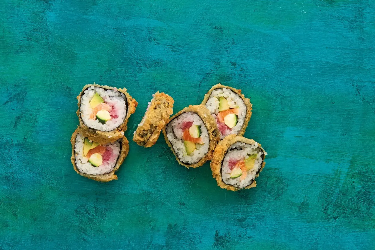 Chrupiące sushi w panko z łososiem i awokado na turkusowym tle.
