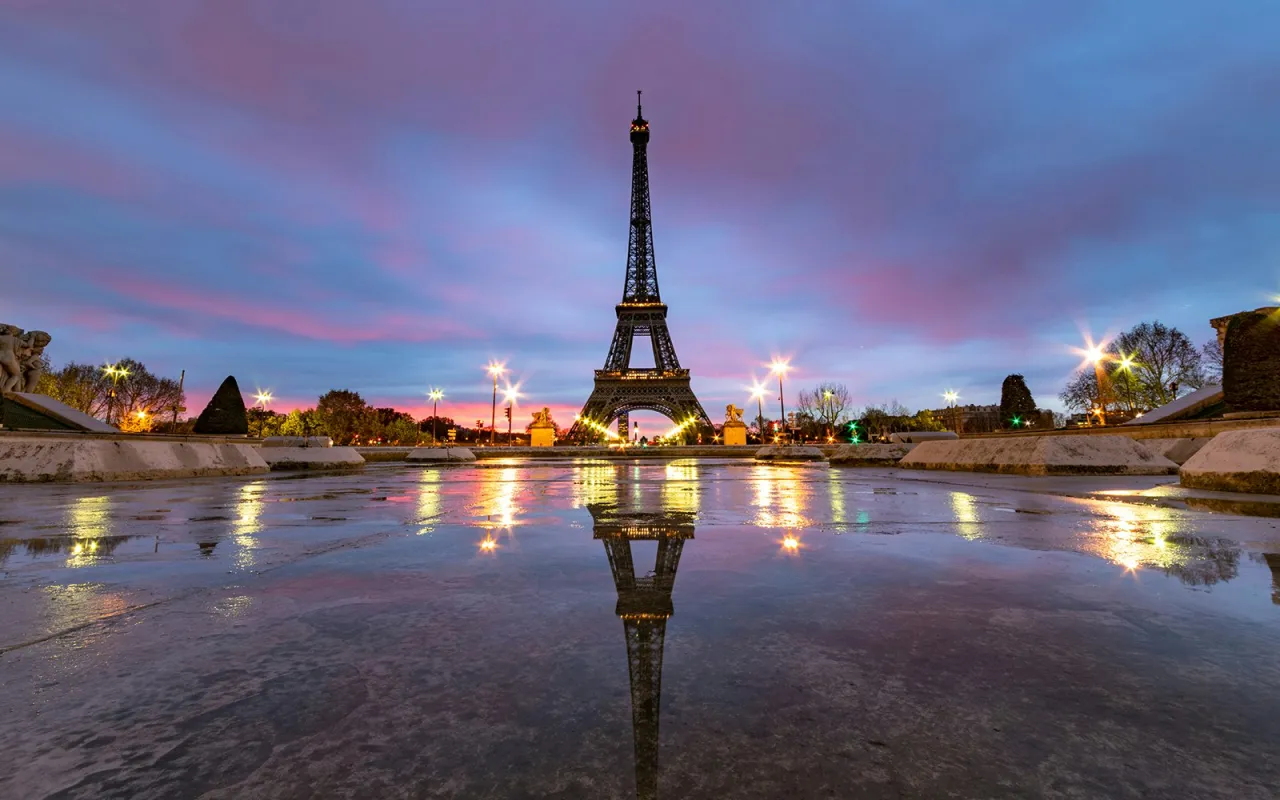 Wieża Eiffla o zmierzchu, odbijająca się w mokrej nawierzchni. Zastanawiasz się, ile kosztuje wejście na wieżę Eiffla?