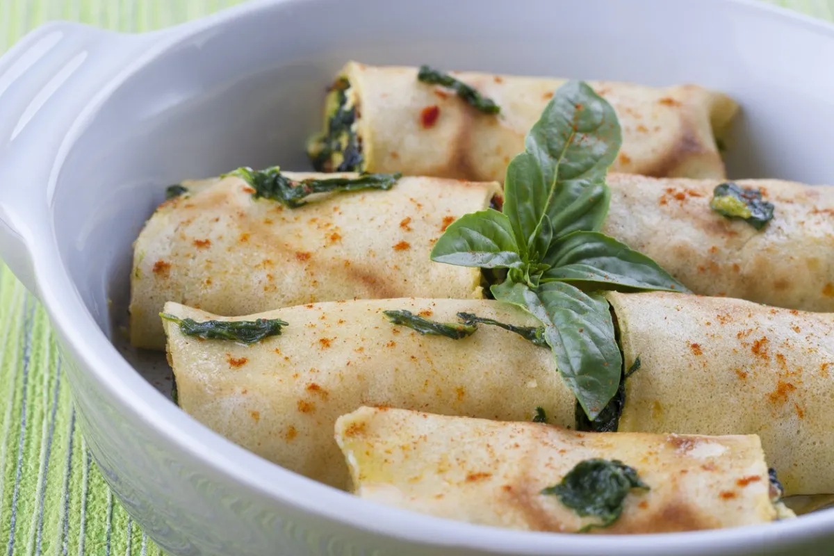 Roladki z mrożonego szpinaku w naleśnikach, posypane papryką, ozdobione bazylią. Prosty spos&oacute;b, jak przyrządzić szpinak mrożony.