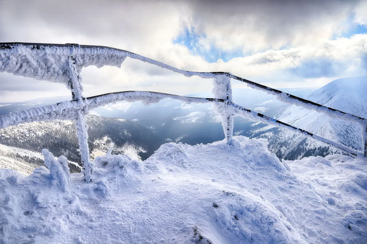 Mroźny krajobraz, gdzie leżą Karkonosze. Lodem pokryta barierka na tle ośnieżonych g&oacute;r i nieba.