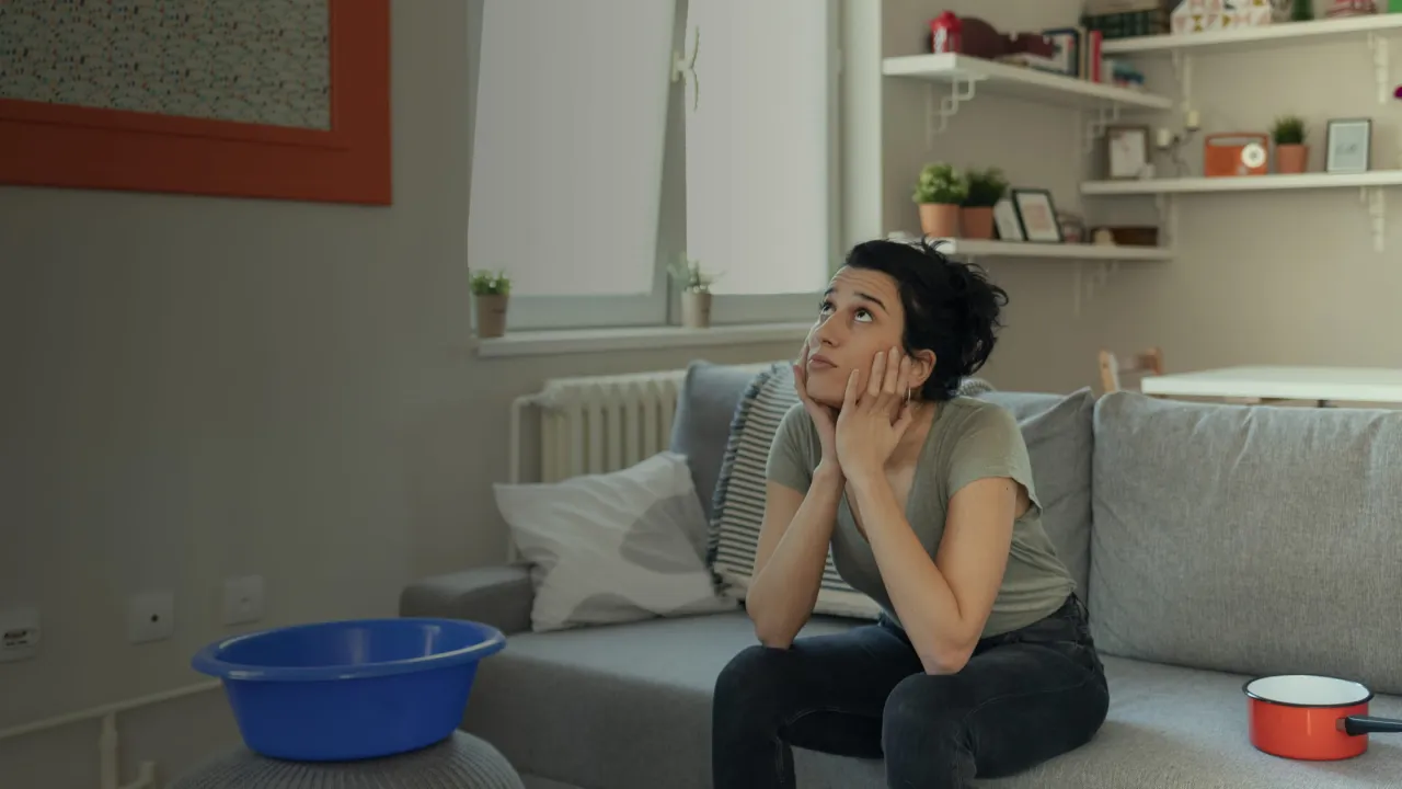 Zmartwiona kobieta siedzi na kanapie z miską i garnkiem, zastanawiając się, co zrobić z uciążliwym sąsiadem w bloku.