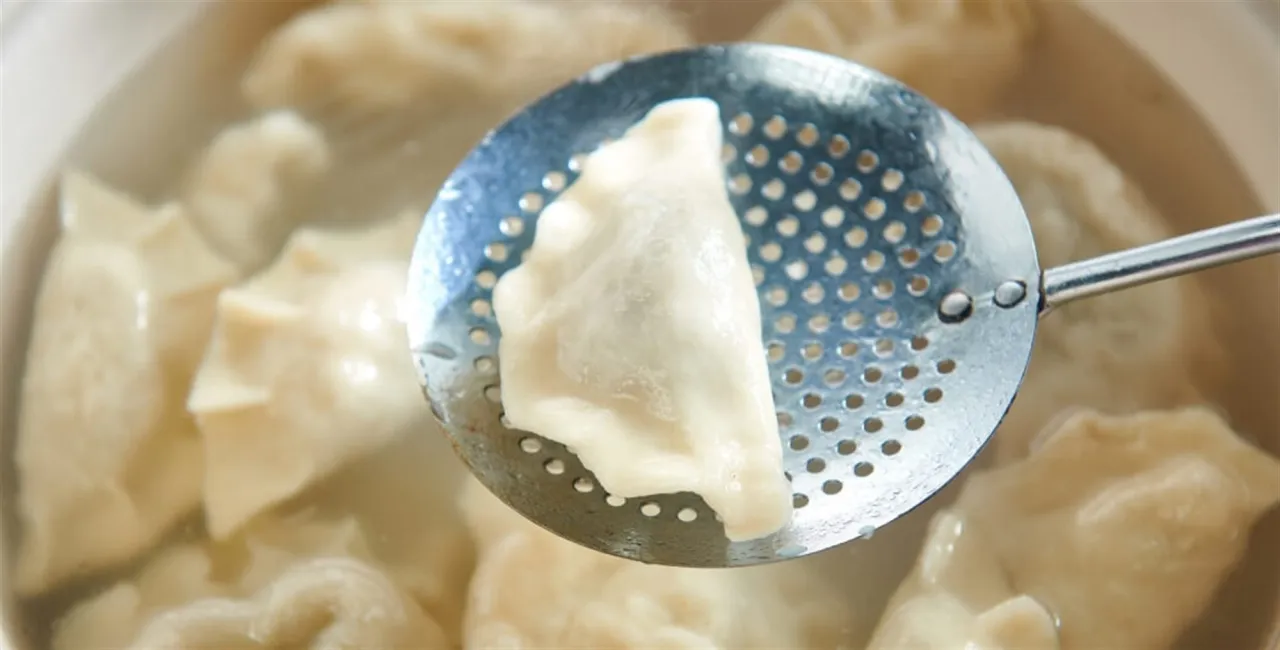 Pierogi gotują się w wodzie. Łyżka cedzakowa wyciąga jednego, pokazując, jak ugotować pierogi do perfekcji.