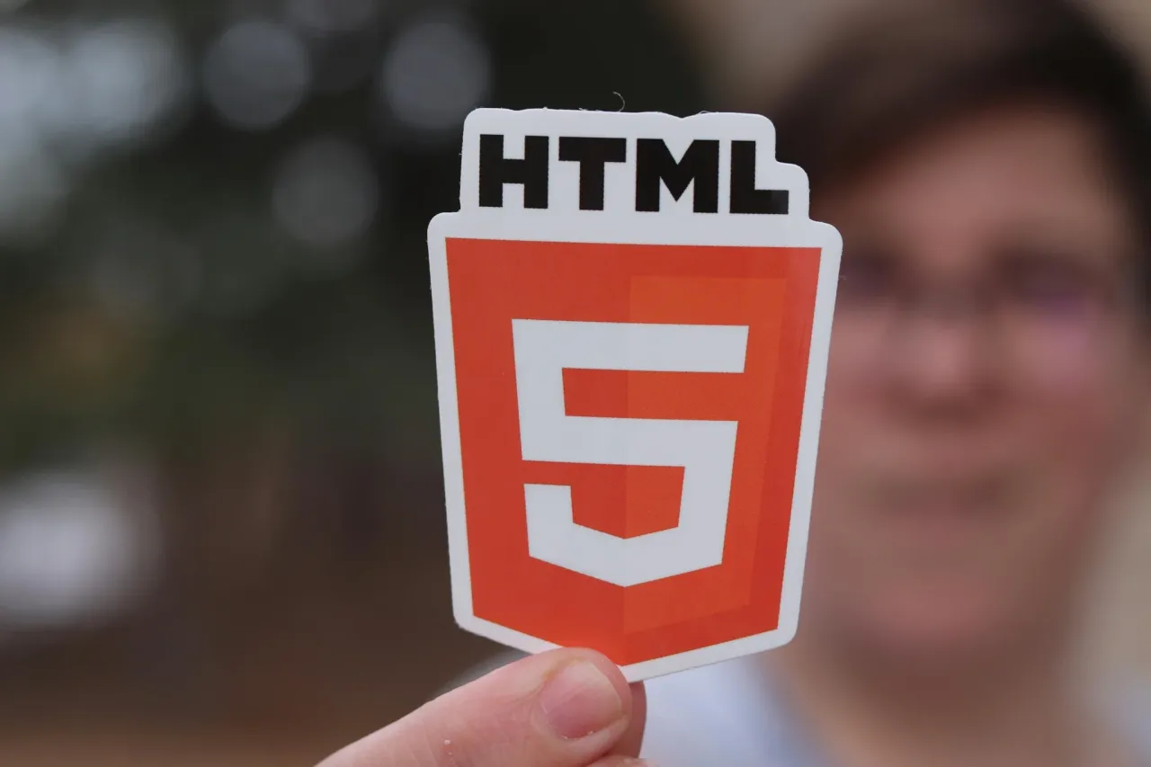 Osoba trzyma naklejkę z logo HTML5, idealną do nauki, jak zacząć stronę html.