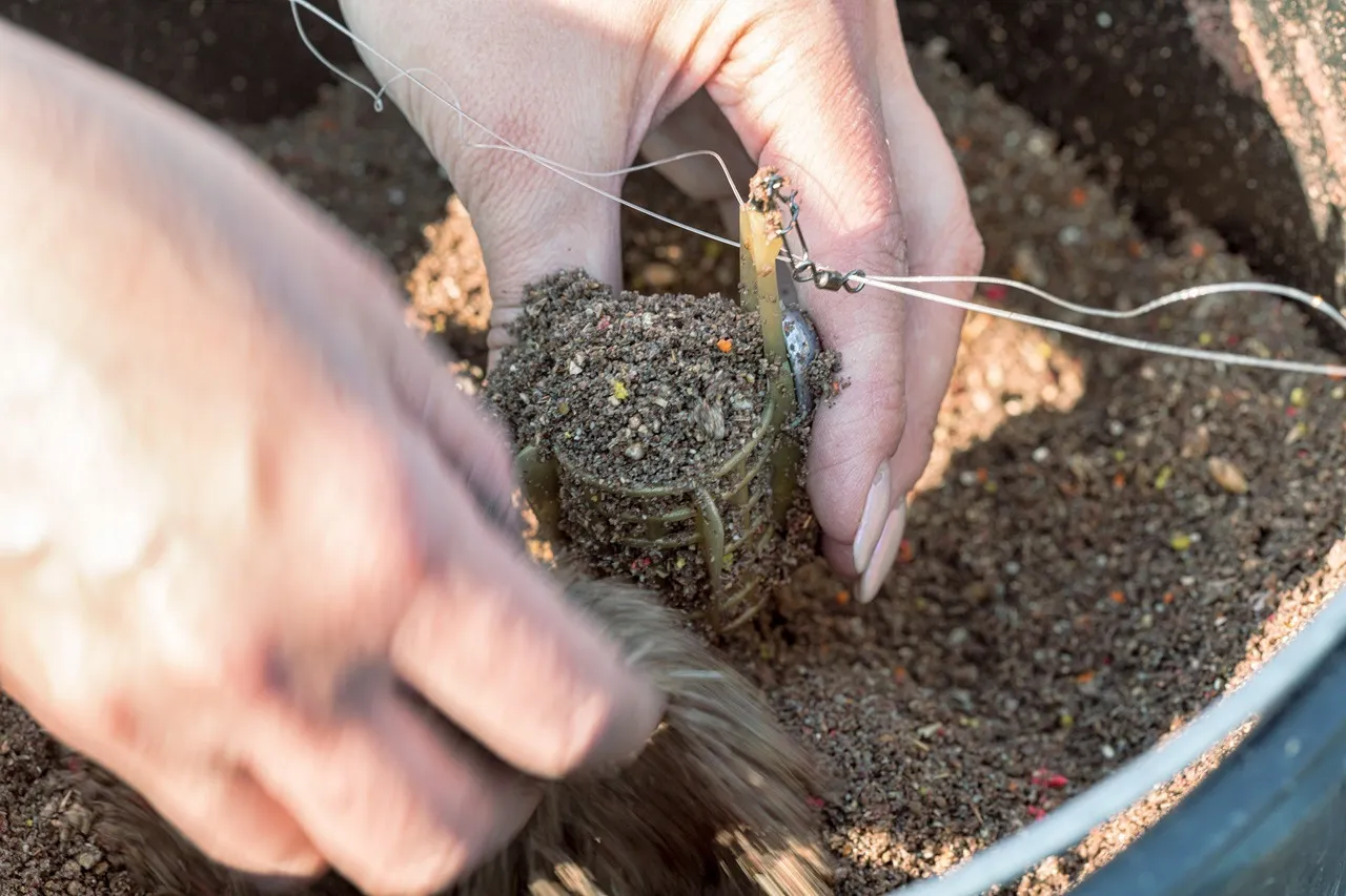 Ręce przygotowują glinę do zanęty, wciskając ją do podajnika wędkarskiego.