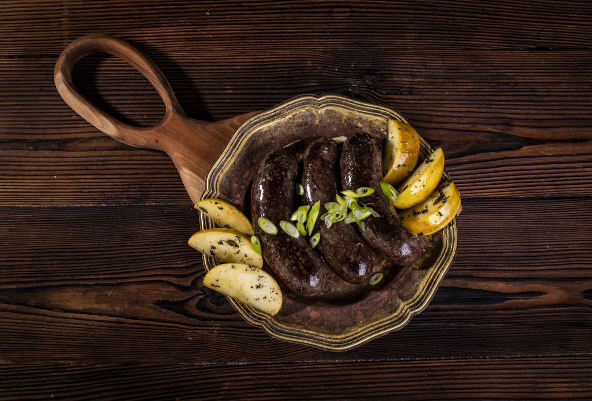 Kaszanka pieczona w piekarniku z ziemniakami i szczypiorkiem, podana na ozdobnym talerzu.