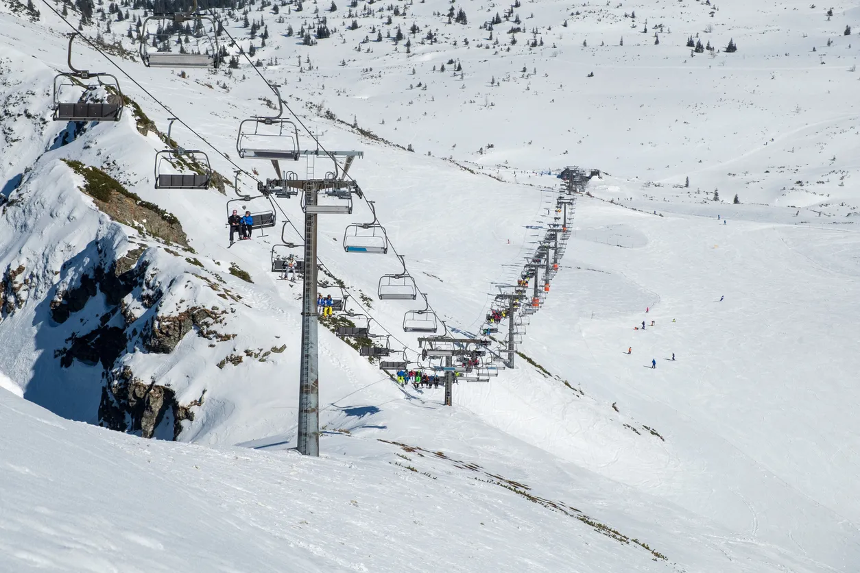 Kolejka krzesełkowa na tle ośnieżonych stoków, gdzie widać narciarzy. Idealne miejsce na czarne trasy narciarskie w Polsce.