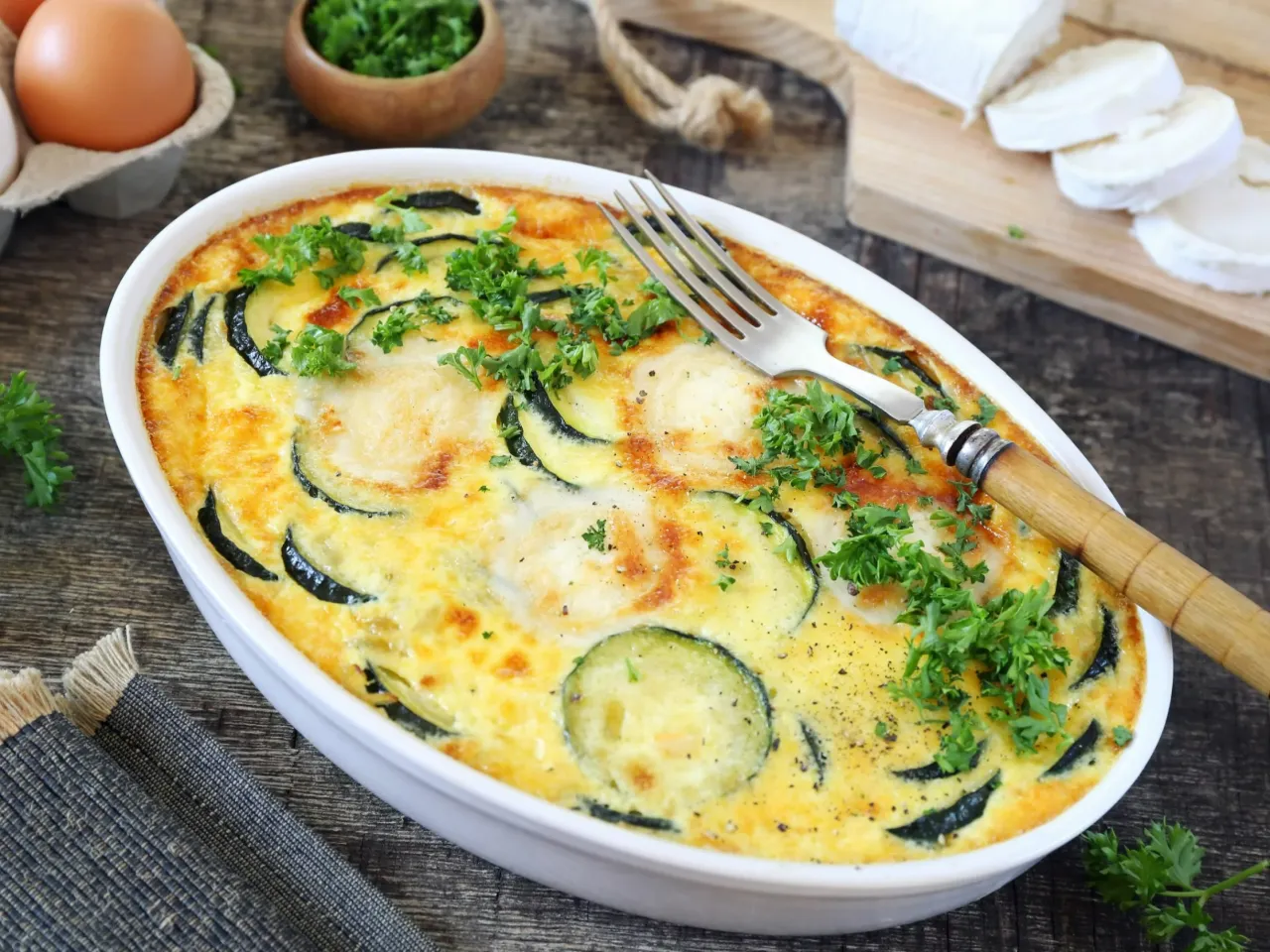 Pyszne zapiekane plastry cukinii z jajkiem i serem, idealne jako pomysł na obiad z cukinią. Posypane świeżą natką pietruszki.