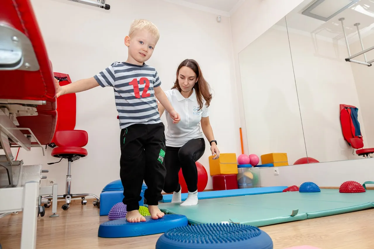 Terapeuta SI pracujący z dzieckiem w sali sensorycznej, z huśtawkami i różnymi teksturami