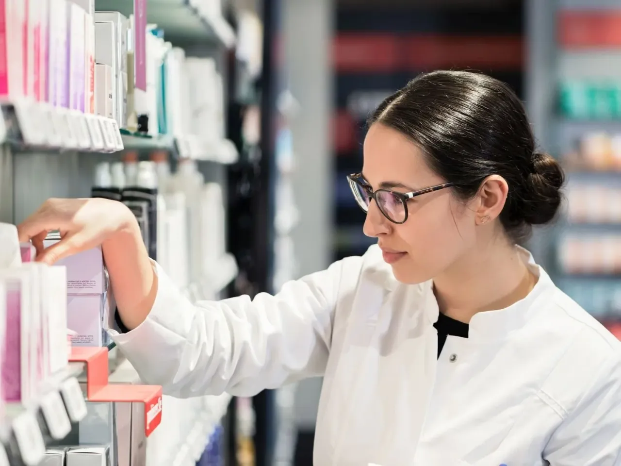 Farmaceutka w okularach wybiera produkt z półki. Dowiaduje się, co to jest ryczałt na recepcie, szukając informacji.